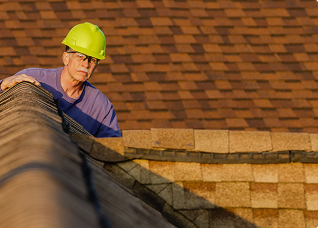 Man inspecting roof wearing yellow hard hat.