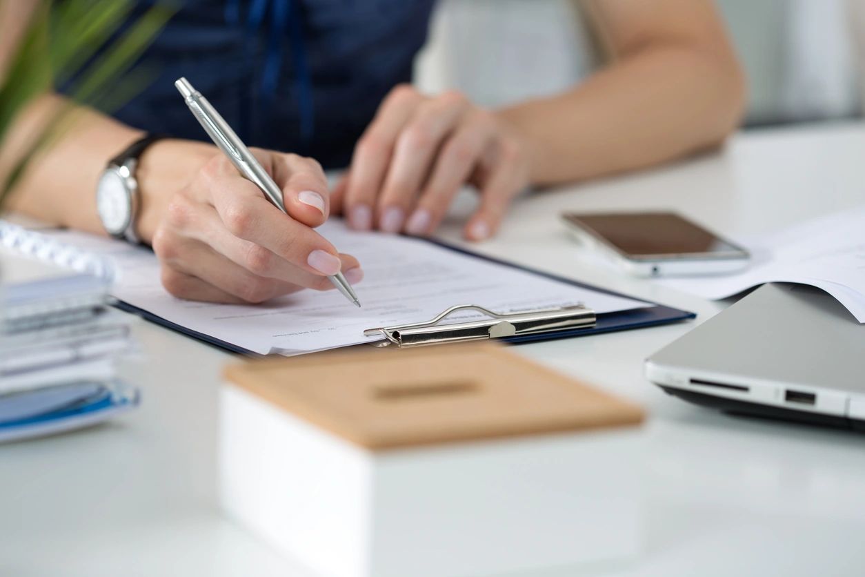Person filling out a form on a clipboard at a desk with office supplies.