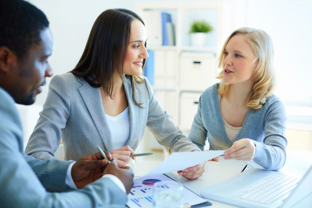Three professionals discussing documents in a bright office setting.