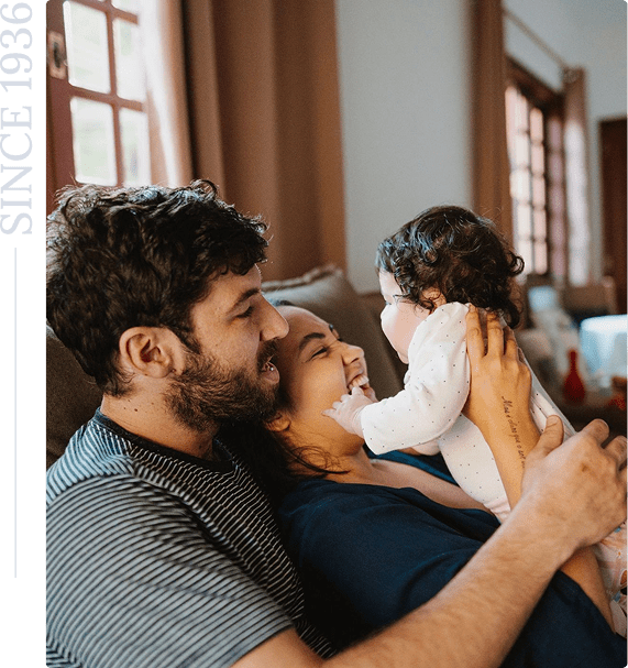 Family smiling and holding a baby indoors.