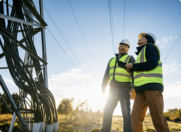 Workers inspecting electrical tower in sunlight.
